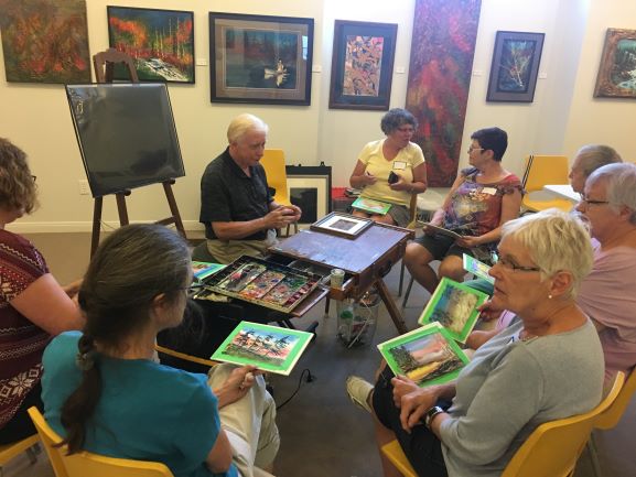 Students sit around Jack Lockhart holding onto their paintings